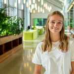 Student met blond haar en wit shirt, veel planten als achtergrond